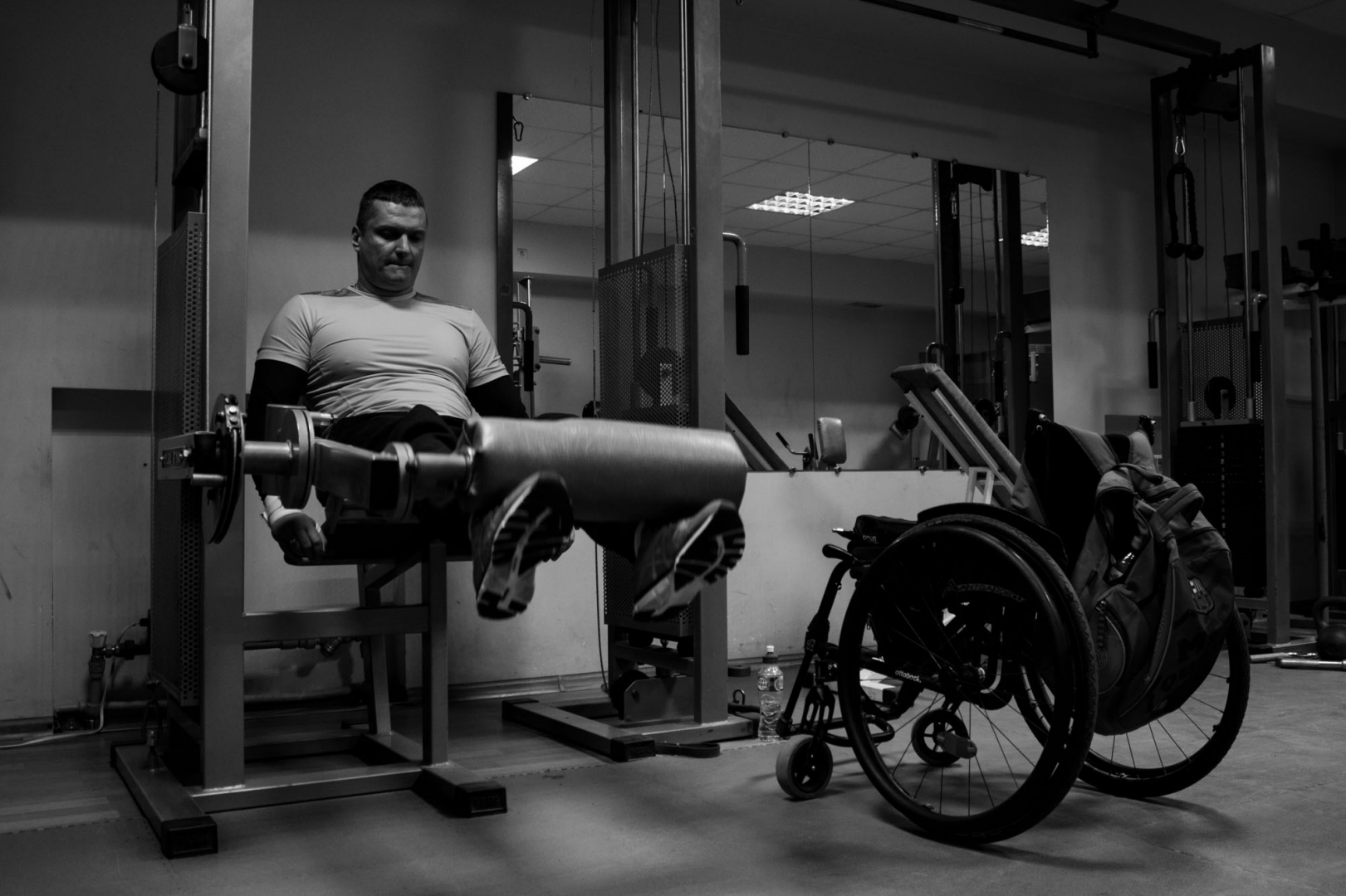Андрей Кожемякин выполняет упражнение на разгибание ног на тренажере для проработки передней поверхности бедра. Из-за травмы у Андрея отсутствует чувствительность в ногах, но благодаря ежедневным тренировкам он может поднимать минимальный вес