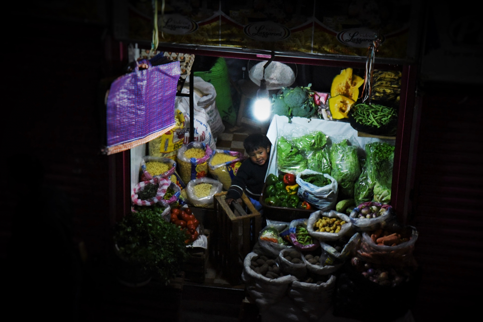 Мальчик за овощным прилавком на вечернем рынке в Ла Пасе. Боливия