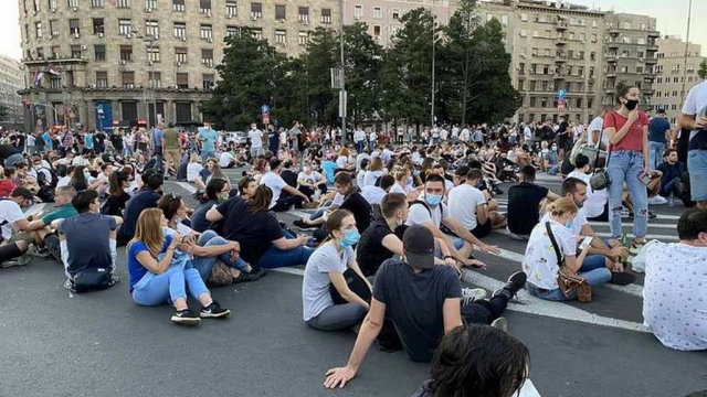 Протестующие сидят на земле перед зданием Национального собрания Сербии, показывая, что они не хотят насилия и беспорядков 